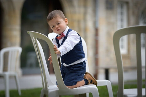 Jeune enfant en tenue élégante jouant sur une chaise pendant le vin d’honneur d’un mariage