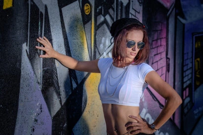 Portrait d’une femme en extérieur devant un mur graffiti, pose dynamique avec lunettes de soleil et éclairage au flash